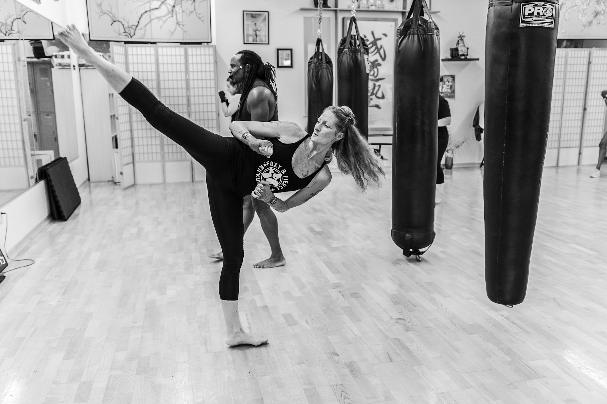 Woman performing a powerful high kick during training at Foxy & Fierce
